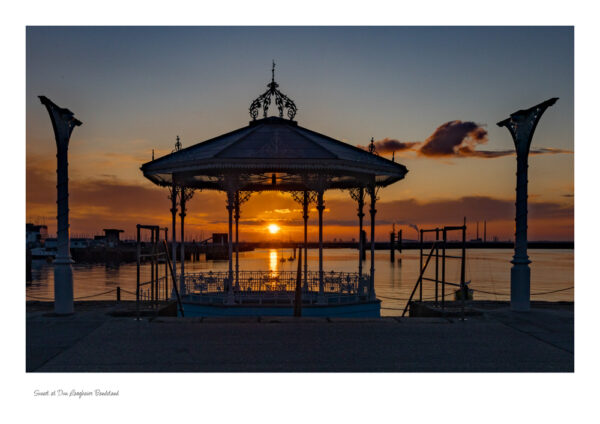 The Victorian Bandstand in Dun Laoghaire with a beautiful red sky and the sun setting in the centre of the bandstand and the pillares on either side of the bandstand.