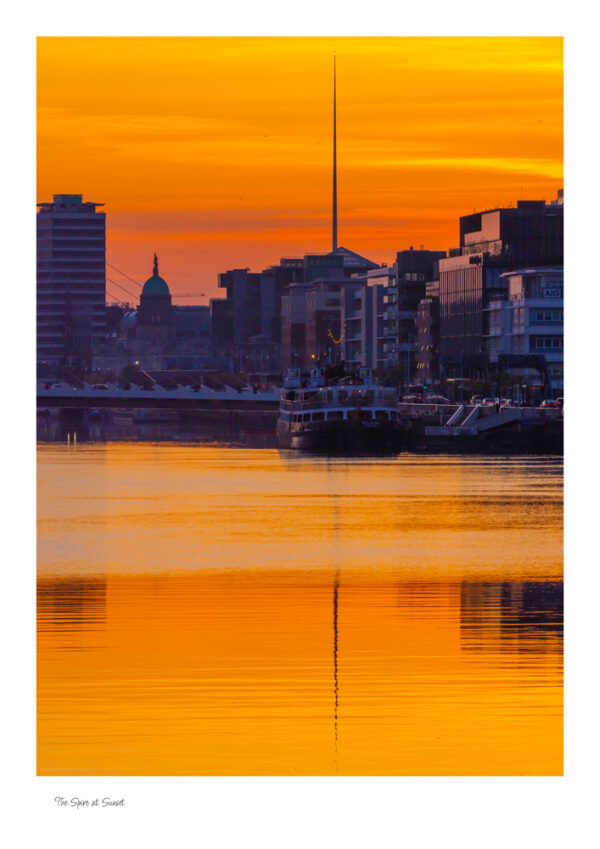 The Spire at Sunset shows the river liffey with the four courts and the spire in the background and a lovely golden sunset sky